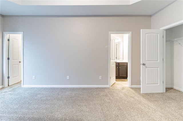 unfurnished bedroom featuring baseboards, a closet, ensuite bathroom, and light colored carpet