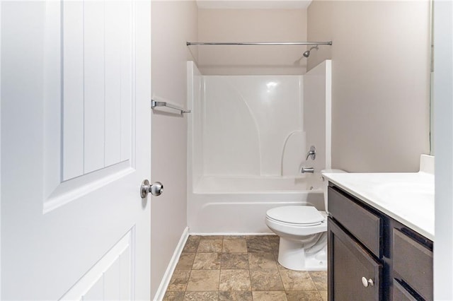 full bath with toilet, vanity, baseboards, stone finish flooring, and washtub / shower combination