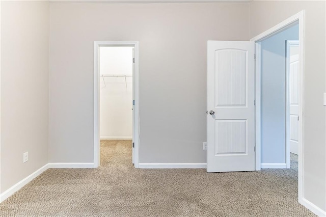 unfurnished bedroom featuring a closet, carpet flooring, a spacious closet, and baseboards