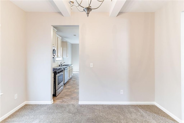 kitchen featuring stainless steel appliances, beamed ceiling, and light colored carpet