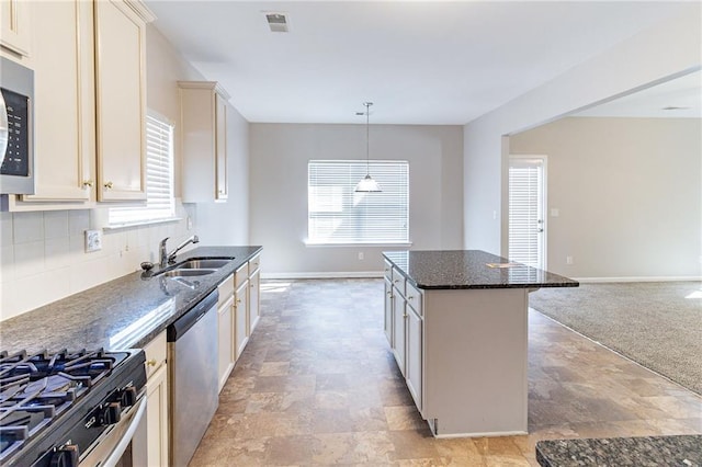 kitchen featuring a center island, backsplash, appliances with stainless steel finishes, a sink, and dark stone countertops