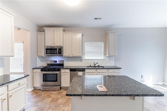 kitchen with visible vents, dark stone countertops, stainless steel appliances, white cabinetry, and a sink