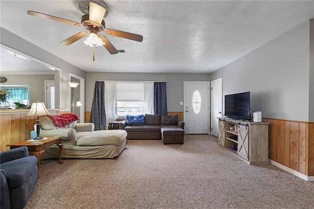 living room featuring carpet flooring, ceiling fan, a textured ceiling, and wood walls