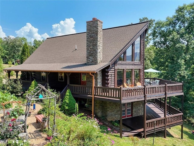 back of property with roof with shingles, a wooden deck, log siding, a chimney, and stone siding