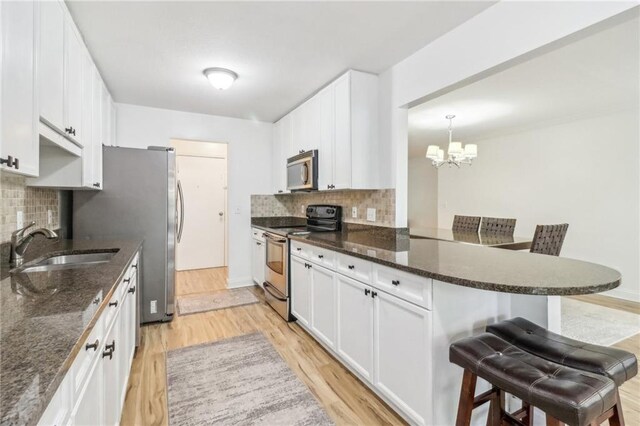 kitchen featuring a kitchen bar, white cabinetry, decorative light fixtures, stainless steel appliances, and kitchen peninsula