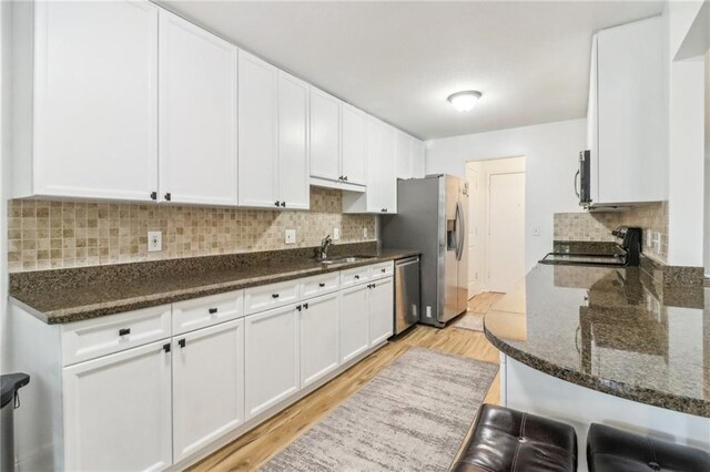 kitchen featuring light wood-type flooring, stainless steel appliances, tasteful backsplash, dark stone countertops, and white cabinets