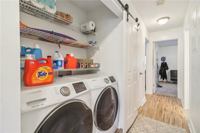 clothes washing area featuring light wood-type flooring, independent washer and dryer, and a barn door