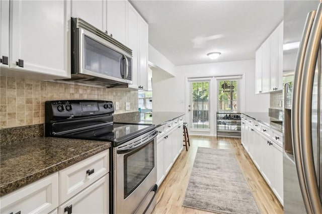 kitchen featuring dark stone countertops, light hardwood / wood-style floors, stainless steel appliances, and white cabinets