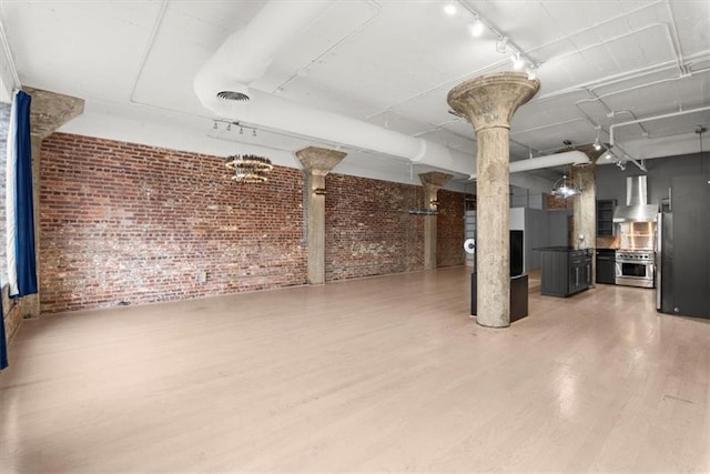 basement with hardwood / wood-style flooring, track lighting, brick wall, and stainless steel fridge