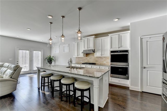 kitchen featuring a sink, under cabinet range hood, open floor plan, gas stovetop, and double oven