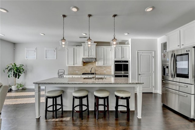 kitchen with a sink, decorative backsplash, under cabinet range hood, appliances with stainless steel finishes, and a kitchen breakfast bar