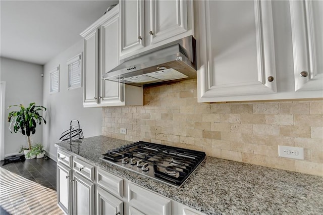 kitchen with tasteful backsplash, light stone countertops, under cabinet range hood, stainless steel gas cooktop, and white cabinetry