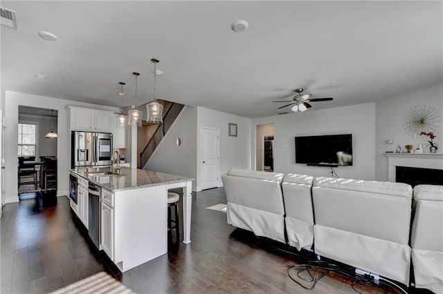 kitchen with dark wood finished floors, open floor plan, light stone counters, a kitchen breakfast bar, and stainless steel appliances