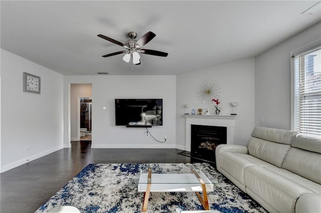 living area with visible vents, ceiling fan, baseboards, dark wood finished floors, and a fireplace with flush hearth
