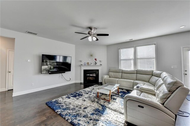 living room featuring wood finished floors, visible vents, baseboards, a fireplace, and ceiling fan