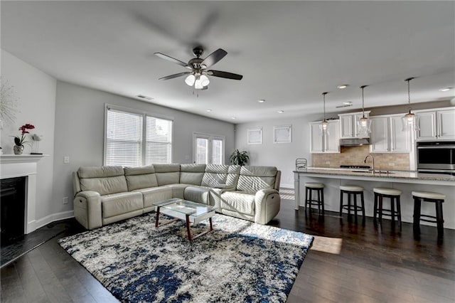 living area featuring visible vents, baseboards, dark wood finished floors, a fireplace, and a ceiling fan