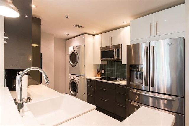 kitchen featuring sink, appliances with stainless steel finishes, stacked washer / dryer, white cabinets, and decorative backsplash