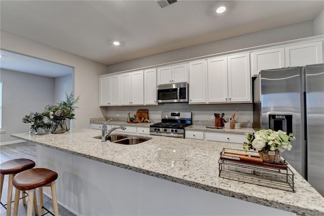 kitchen featuring sink, white cabinets, light stone counters, hardwood / wood-style flooring, and appliances with stainless steel finishes