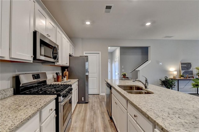 kitchen with stainless steel appliances, light wood-type flooring, light stone countertops, sink, and white cabinetry