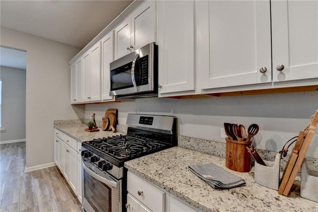 kitchen with stainless steel appliances, white cabinetry, light wood-type flooring, and light stone countertops