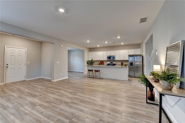 kitchen with stainless steel appliances, light hardwood / wood-style flooring, a kitchen breakfast bar, and white cabinetry