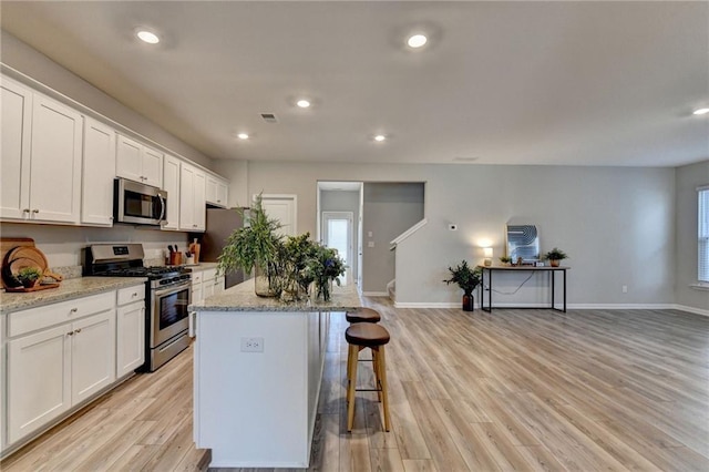 kitchen featuring stainless steel appliances, white cabinets, a center island, and light stone countertops