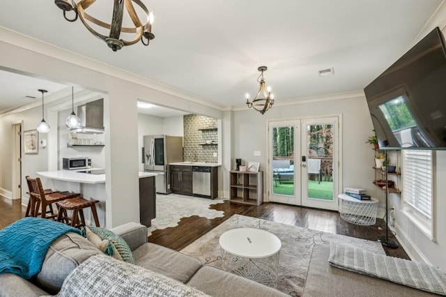 living room with a wealth of natural light, wood-type flooring, ornamental molding, and a chandelier