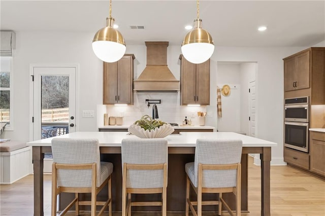 kitchen with premium range hood, stainless steel double oven, a center island, and hanging light fixtures