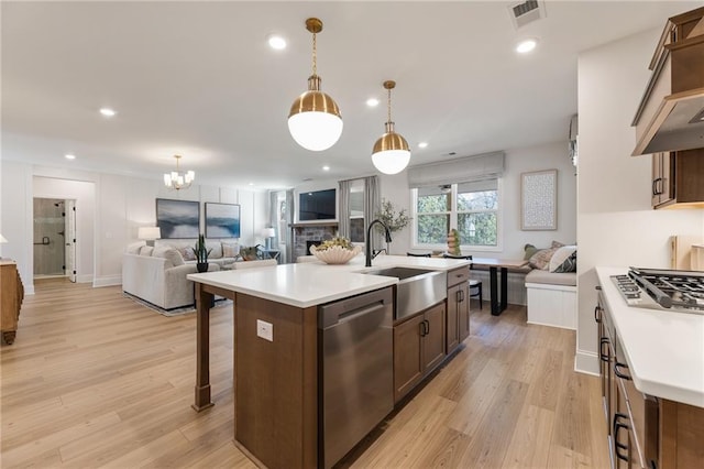 kitchen featuring sink, hanging light fixtures, appliances with stainless steel finishes, an island with sink, and light hardwood / wood-style floors