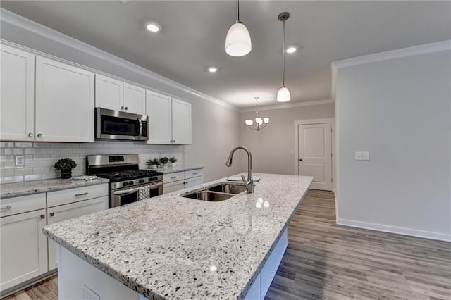 kitchen featuring a center island with sink, ornamental molding, a sink, stainless steel appliances, and backsplash