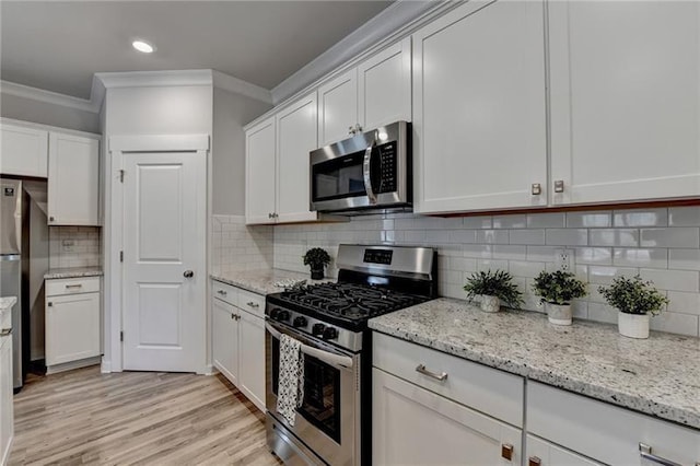 kitchen featuring white cabinets, light wood finished floors, stainless steel appliances, and backsplash