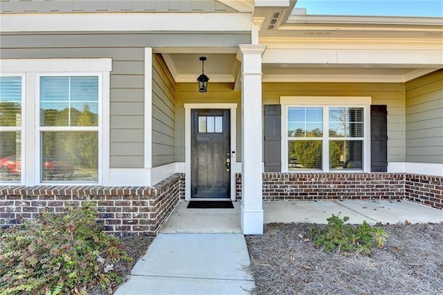 view of exterior entry featuring covered porch and brick siding