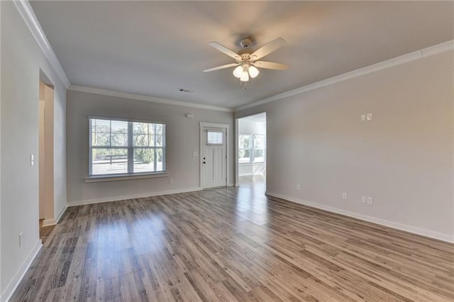 empty room featuring plenty of natural light, crown molding, baseboards, and wood finished floors