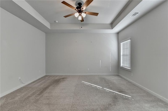 carpeted spare room featuring baseboards, visible vents, a tray ceiling, and a ceiling fan