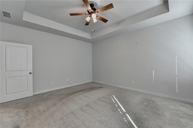 carpeted empty room with ceiling fan, a tray ceiling, visible vents, and baseboards