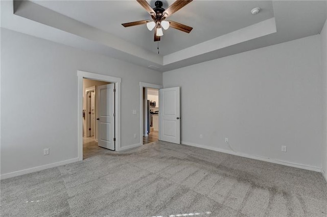 unfurnished bedroom with a ceiling fan, carpet, a raised ceiling, and baseboards