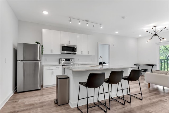 kitchen with white cabinets, light hardwood / wood-style flooring, stainless steel appliances, and an island with sink