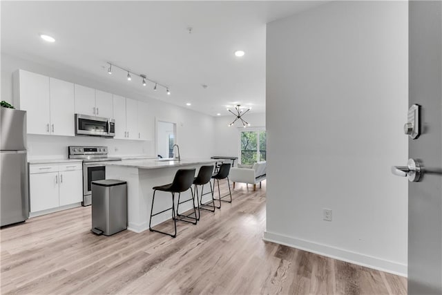 kitchen with white cabinetry, stainless steel appliances, light hardwood / wood-style floors, and an island with sink