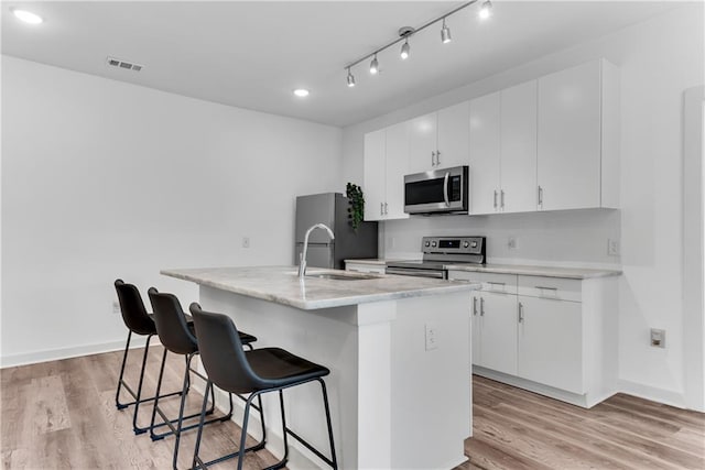 kitchen featuring appliances with stainless steel finishes, light hardwood / wood-style flooring, white cabinets, and a center island with sink