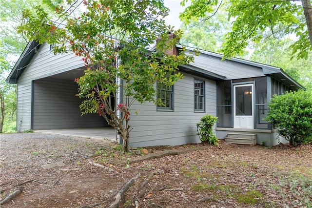 view of front of house with dirt driveway, entry steps, a carport, a sunroom, and a chimney