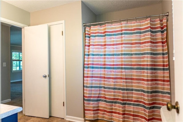 full bathroom featuring a textured ceiling, curtained shower, and baseboards