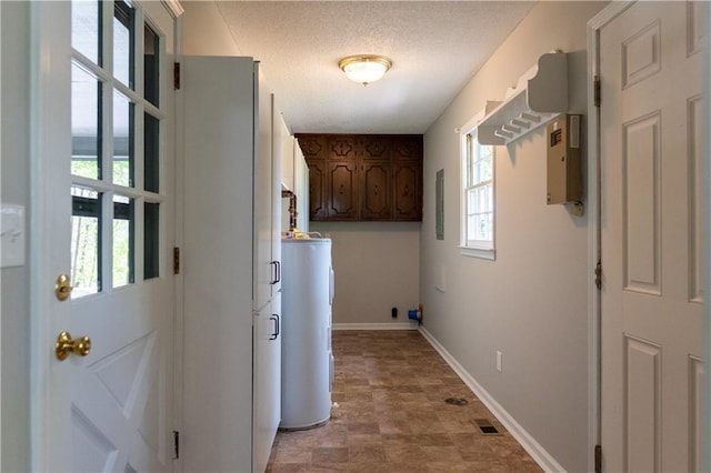 laundry room with electric water heater, healthy amount of natural light, cabinet space, baseboards, and a textured ceiling