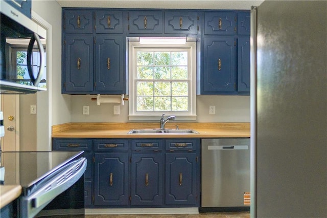 kitchen featuring appliances with stainless steel finishes, a sink, and blue cabinets
