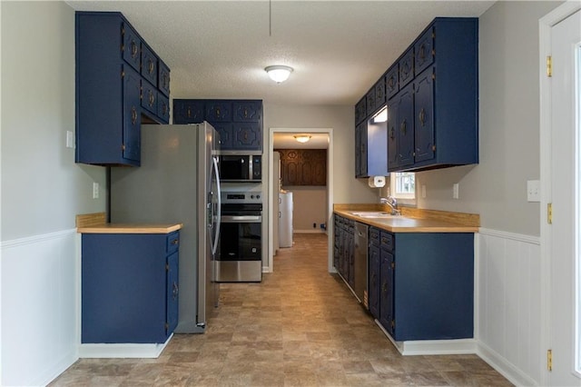 kitchen featuring blue cabinets, appliances with stainless steel finishes, a sink, light countertops, and a textured ceiling