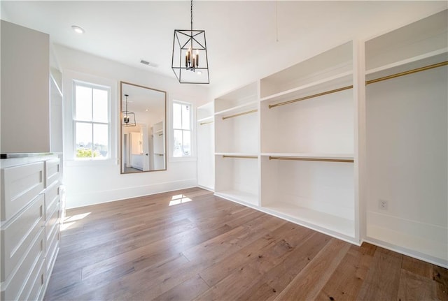 spacious closet with wood-type flooring and an inviting chandelier