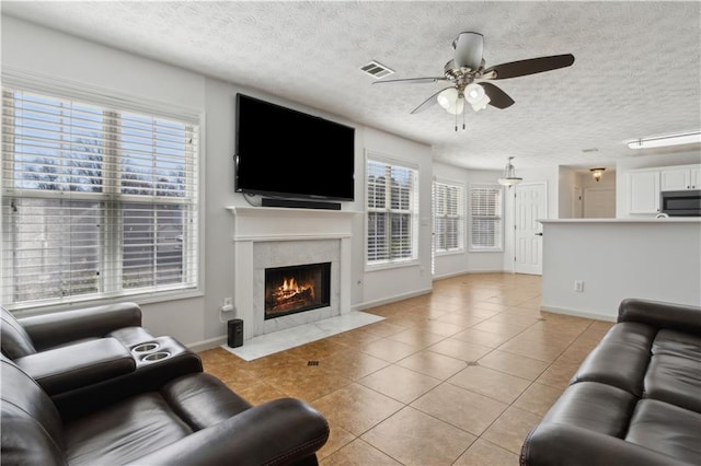 living area featuring visible vents, a premium fireplace, light tile patterned flooring, a textured ceiling, and a ceiling fan