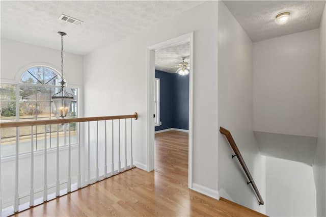 hallway with visible vents, an upstairs landing, a textured ceiling, wood finished floors, and an inviting chandelier