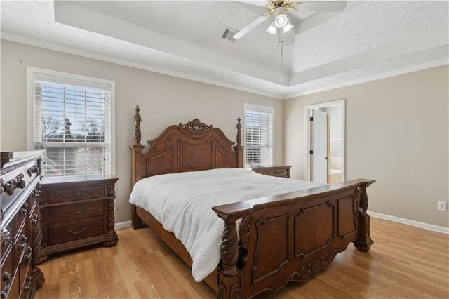 bedroom with a tray ceiling, light wood-style floors, and visible vents