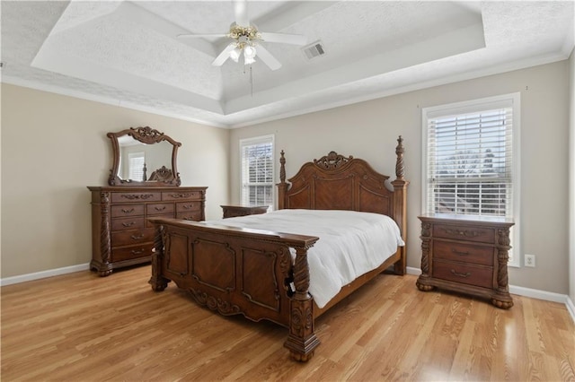 bedroom with light wood-style flooring, a textured ceiling, a raised ceiling, and baseboards