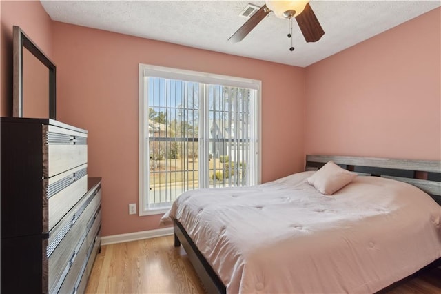 bedroom with visible vents, a ceiling fan, a textured ceiling, wood finished floors, and baseboards